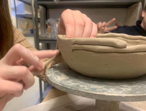 Billedet viser en elev der i gang med at dreje ler på keramikværksted